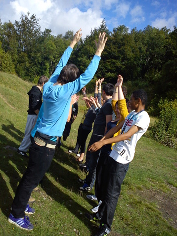 A group of young people outdoors on a hillside, arms raised together during a group exercise
